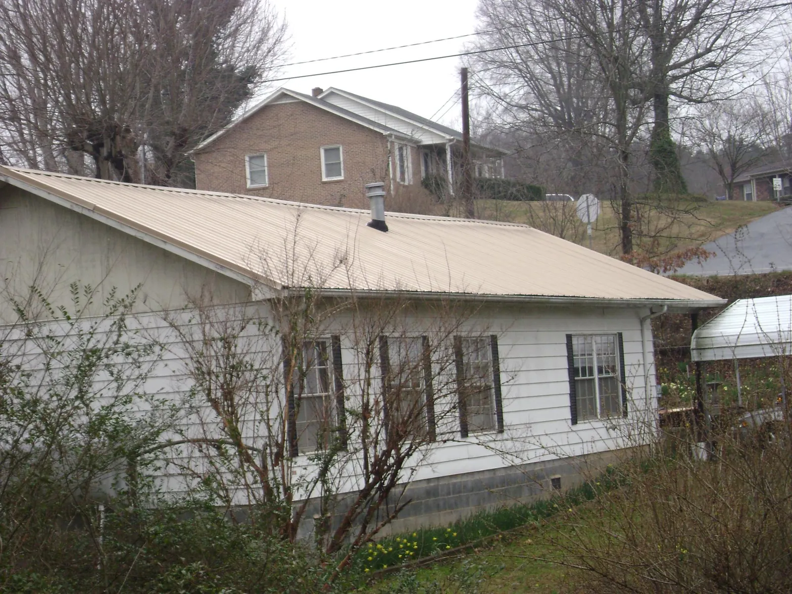 Tan metal roof on a white sided house set into a hillside — Commercial Roofing by Roofing Brothers in Lismore